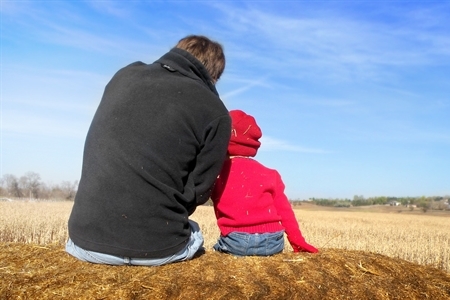 Ein Vater sitzt mit seinem Sohn auf einem Feld